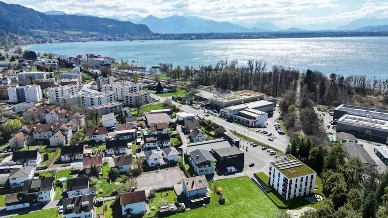 Eine Luftaufnahme zeigt die Wohngegend am Seeufer mit Bergen im Hintergrund und einem Neubau.