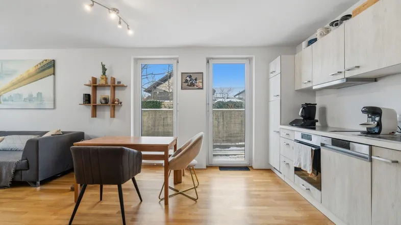 Heller offener Wohn- und Essbereich mit integrierter Küche und Zugang zum Balkon.