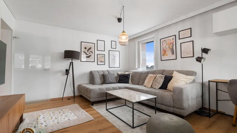 Helles Wohnzimmer mit modernem Ecksofa, Holzboden und stilvoller Wanddekoration.