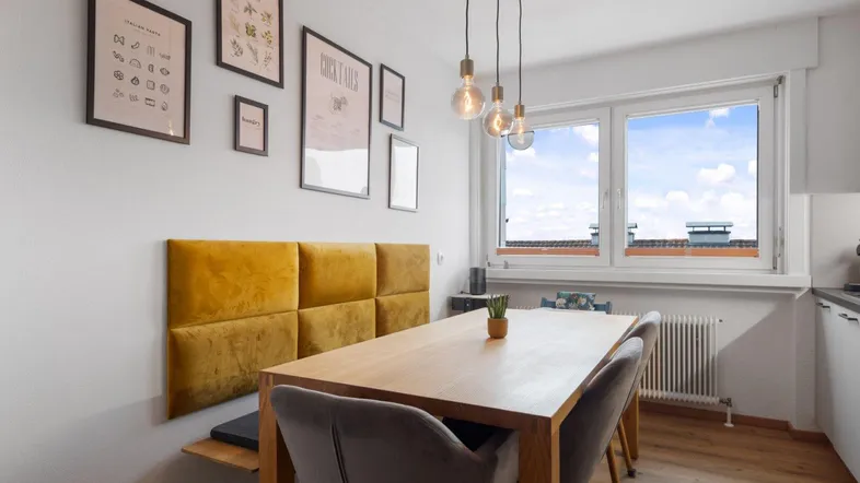 Heller Essbereich in der Küche mit Holztisch, gelber Sitzbank und Blick nach draußen.