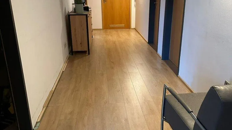 Heller Flur mit Laminatboden, weißen Wänden und mehreren Türen, der einen einladenden Eingangsbereich schafft.