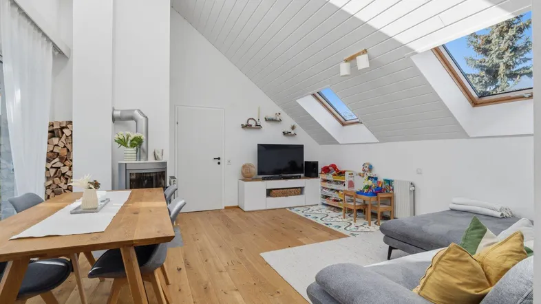 Helles Wohn- und Esszimmer mit Holzboden, Kamin und Dachfenstern, die viel Licht hereinlassen.