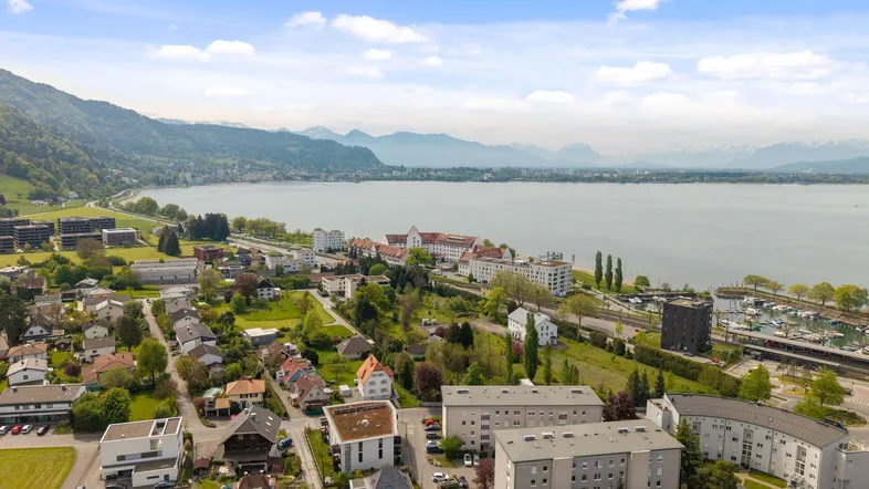 Weitläufige Luftaufnahme einer Stadt am Seeufer mit Wohngebäuden und Bergen.