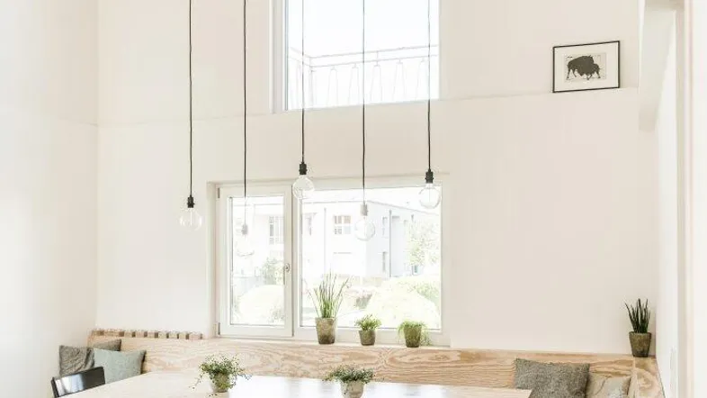 Heller Essbereich mit Holzbänken, hohen Decken und großen Fenstern, die viel Licht hereinlassen.