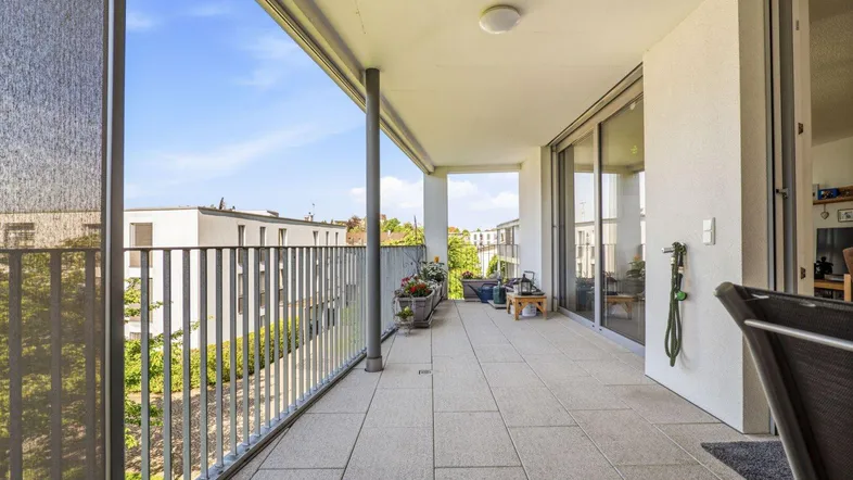 Geräumiger Balkon mit Fliesenboden, Metallgeländer und Blick auf die umliegenden Gebäude und viel Grün.