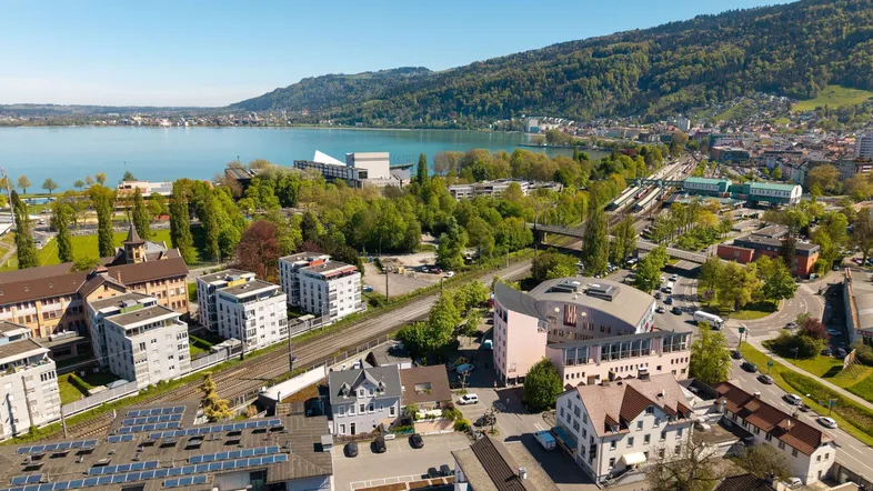 Luftaufnahme einer Stadt am See mit Bergen im Hintergrund und verschiedenen Gebäuden.