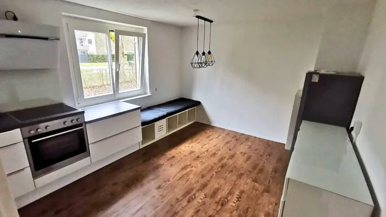 Heller Küchenbereich mit Laminatboden, Fenster und einer praktischen Sitzbank mit Stauraum.