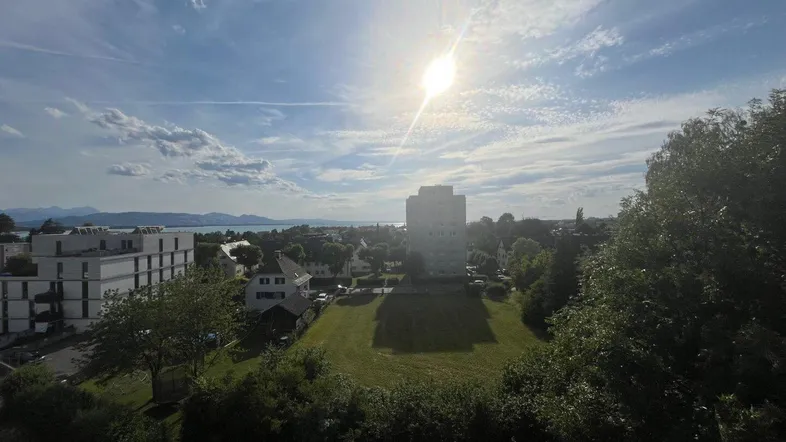 Weitläufiger Blick über die Stadt und den See unter einem sonnigen Himmel mit Wolken.