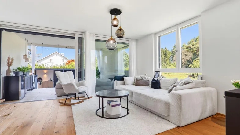 Helles Wohnzimmer mit großem Sofa, Holzboden und direktem Zugang zur Terrasse mit Grünblick.