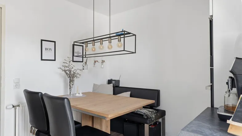 Heller Essbereich mit Holztisch, schwarzen Stühlen und moderner Hängelampe.