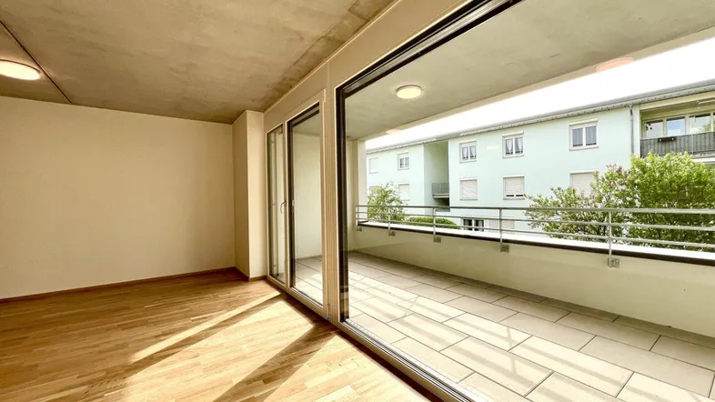 Helles Wohnzimmer mit Parkettboden und Zugang zu einem großen Balkon mit Blick ins Grüne.