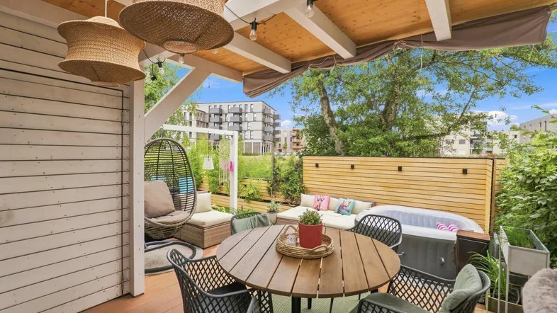 Gemütliche überdachte Terrasse mit Essbereich, Lounge-Möbeln und Whirlpool, umgeben von Grün.