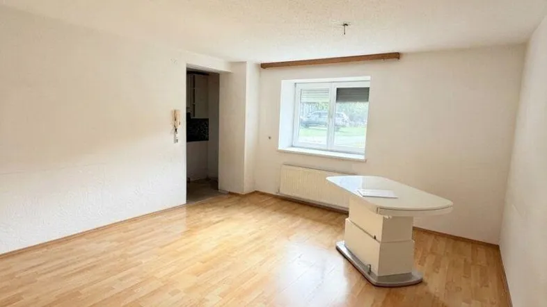 Helles Wohnzimmer mit Laminatboden und einem Fenster, das viel Tageslicht hereinlässt.