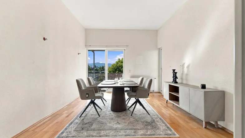 Heller Essbereich mit Holzboden, modernem Esstisch und Zugang zum Balkon mit Bergblick.