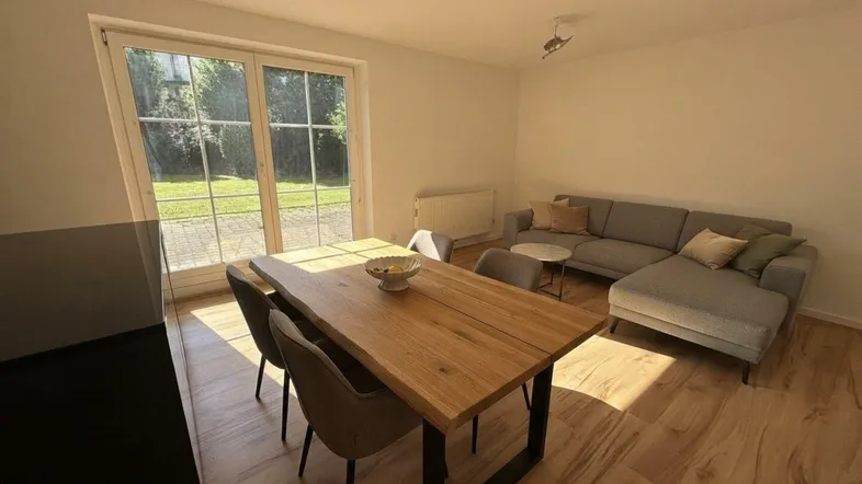 Heller Wohn- und Essbereich mit Holztisch, bequemer Couch und Zugang zum Garten.
