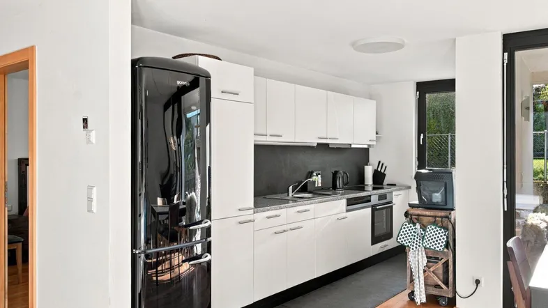 Moderne Küche mit weißen Schränken, schwarzem Kühlschrank und Holzboden.