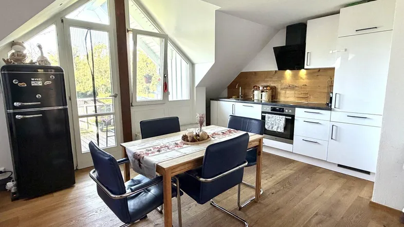 Helle Küche mit Essbereich, modernen weißen Schränken, Holzakzenten und einem Retro-Kühlschrank unter der Dachschräge.