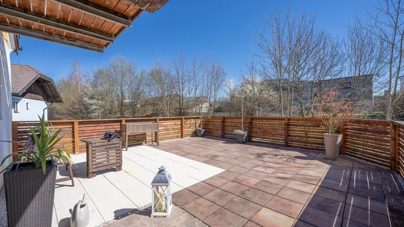 Große, sonnige Terrasse mit Holzzaun, verschiedenen Bodenbelägen und Sitzgelegenheiten im Freien.