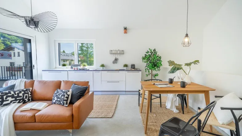 Helles, offenes Wohn-Esszimmer mit integrierter Küche, Ledersofa und Zugang zum Balkon.