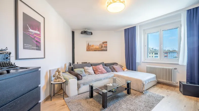 Helles Wohnzimmer mit bequemer Eckcouch, Projektor und Blick auf die Stadt.
