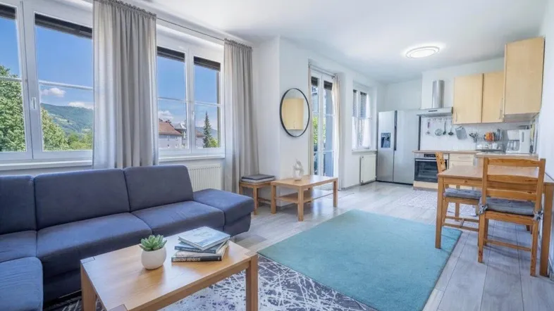 Heller offener Wohn- und Essbereich mit Sofa, Teppich und integrierter Küche mit Bergblick.