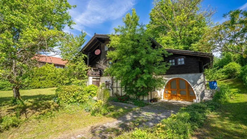 Charmantes Holzhaus mit gewölbtem Garagentor und üppiger grüner Vegetation im Sommer.