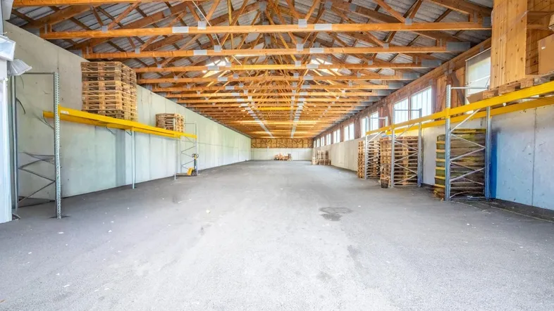 Geräumige Lagerhalle mit hoher Holzdecke, Betonwänden und Regalsystemen, ideal für gewerbliche Nutzung.
