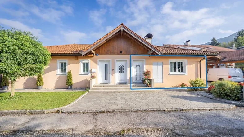 Vorderansicht eines Einfamilienhauses mit zwei Eingängen, gepflastertem Vorplatz und kleinem Vorgarten.