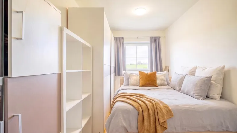 Gemütliches Schlafzimmer mit Einzelbett, Schränken und Blick ins Grüne.