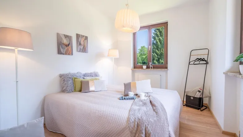 Helles Schlafzimmer mit Holzboden, großem Fenster und gemütlichem Bett, ideal für erholsame Nächte.