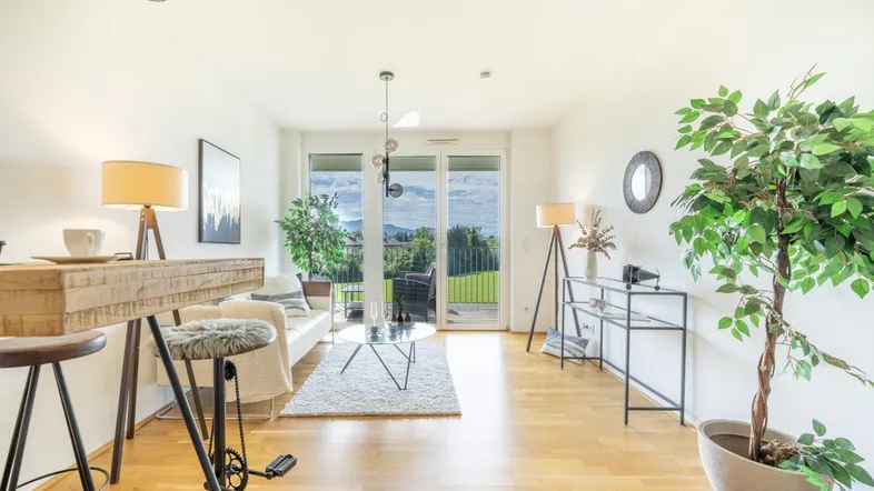 Helles Wohnzimmer mit Holzboden, modernem Mobiliar und Zugang zu einem Balkon mit grüner Aussicht.