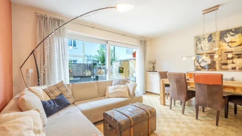 Helles Wohn- und Esszimmer mit Parkettboden, bequemer Couch und Zugang zum Garten.