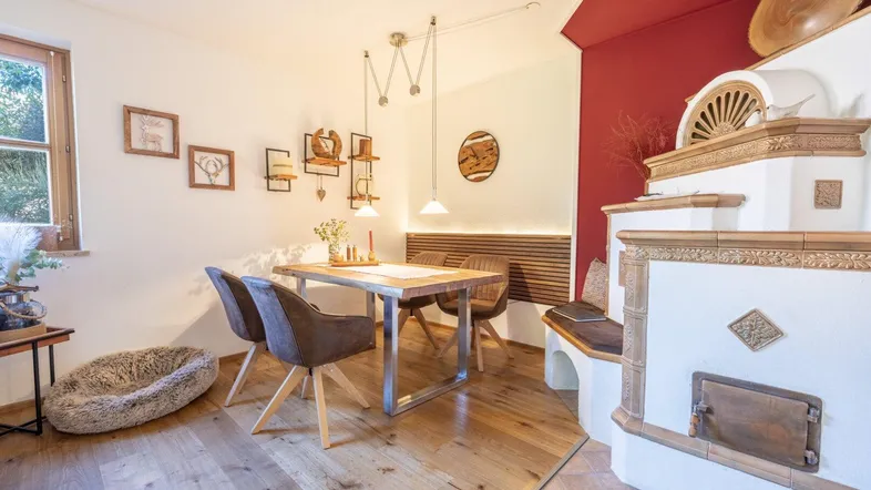 Heller Essbereich mit Holztisch, modernen Stühlen und traditionellem Kachelofen.