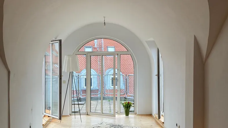 Helles Wohnzimmer mit gewölbter Decke, Holzboden und Zugang zu einem französischen Balkon.