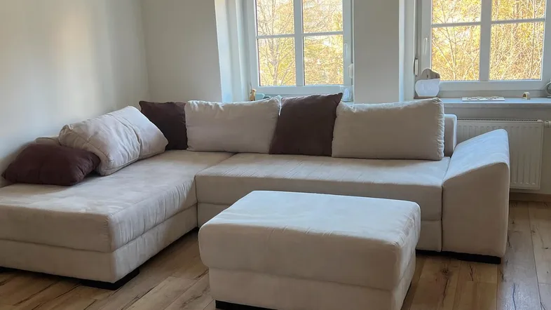 Helles Wohnzimmer mit großem Ecksofa, passendem Hocker und Holzfußboden.