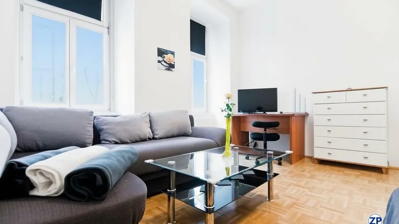 Helles Wohnzimmer mit Sofa, Couchtisch, Schreibtisch und Parkettboden.