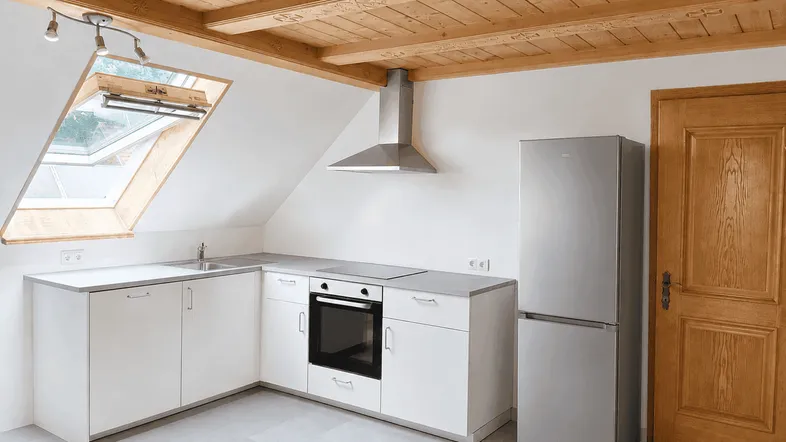 Neue, helle Küche im Dachgeschoss mit weißen Schränken, Holzbalkendecke und Dachfenster.