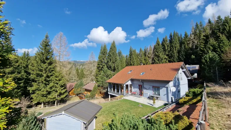 Charmantes Haus in den Bergen mit rotem Ziegeldach und umgebendem Wald unter blauem Himmel.