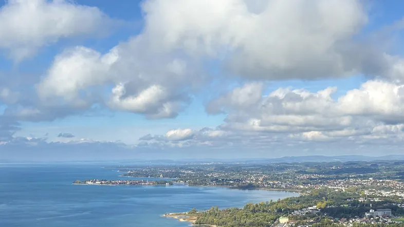 Panoramablick auf den See, die Küstenlinie und die umliegende Stadt mit Bergen im Hintergrund.