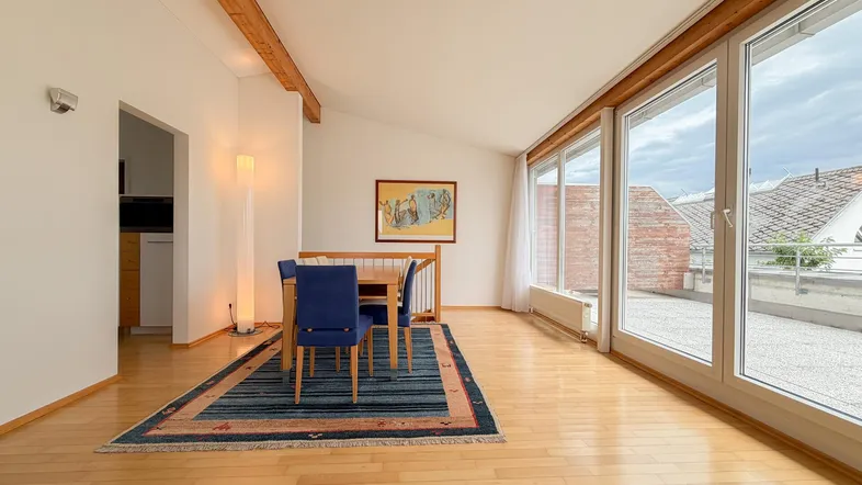 Helles Wohn- und Esszimmer mit Holzbalken, Parkettboden und Zugang zur Dachterrasse.