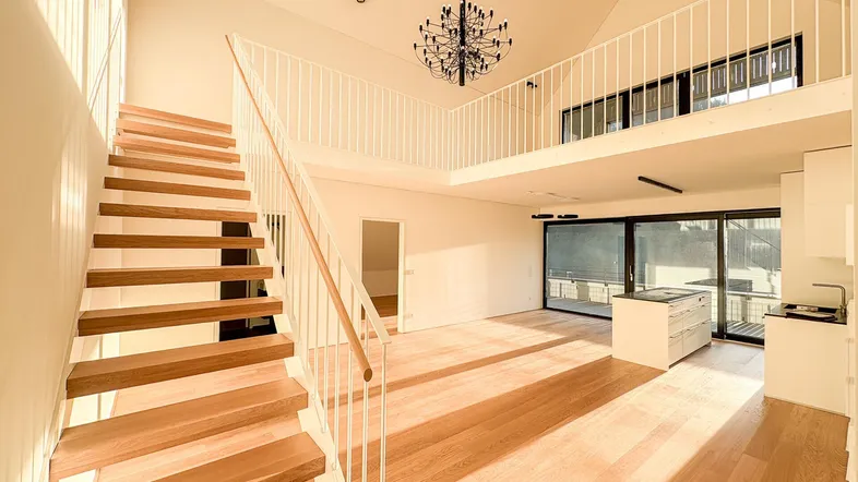 Geräumiger offener Wohnbereich mit moderner Küche, Holztreppe und Galerie im Neubau.