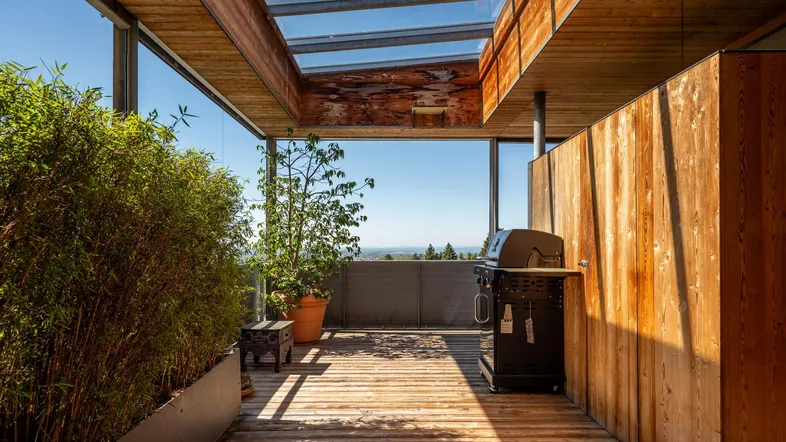 Geräumige Holzterrasse mit Glasdach, Grillbereich und weitem Ausblick ins Grüne.