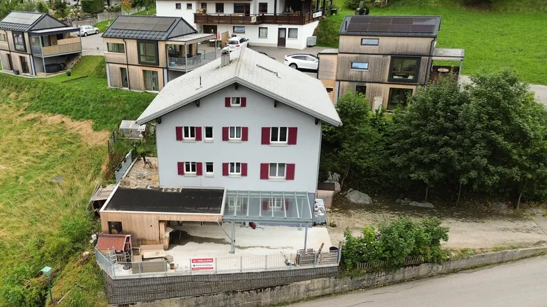 Luftaufnahme eines Hauses mit Satteldach, Carport und umliegender grüner Landschaft.