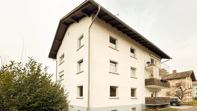 Weißes Mehrfamilienhaus mit mehreren Etagen und Balkonen unter bewölktem Himmel.