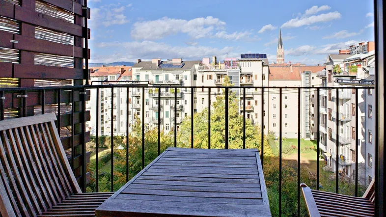 Gemütlicher Balkon mit Holztisch und Stühlen, bietet einen schönen Blick über die Stadt.