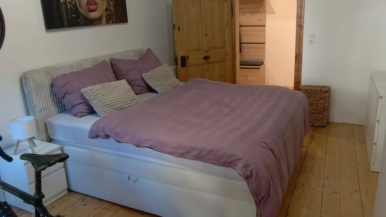 Gemütliches Schlafzimmer mit Holzbalkendecke, Holzboden und einem Fahrradtrainer.