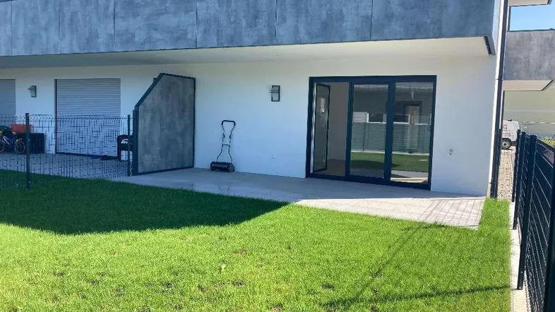 Gepflegter Gartenbereich mit Rasenfläche und angrenzender Terrasse vor einem modernen Gebäude.