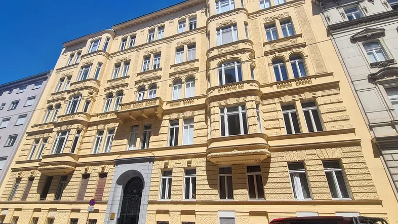 Fassade eines historischen Wohngebäudes mit vielen Fenstern und Erkern unter blauem Himmel.