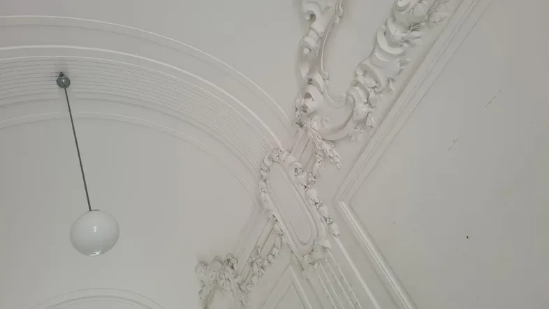 Detailaufnahme einer aufwendig verzierten Stuckdecke mit klassischem Design und Pendelleuchte.