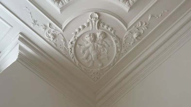 Detailreiche Stuckdecke mit kunstvollen Verzierungen und Engelsmotiven, die den klassischen Stil des Raumes unterstreicht.